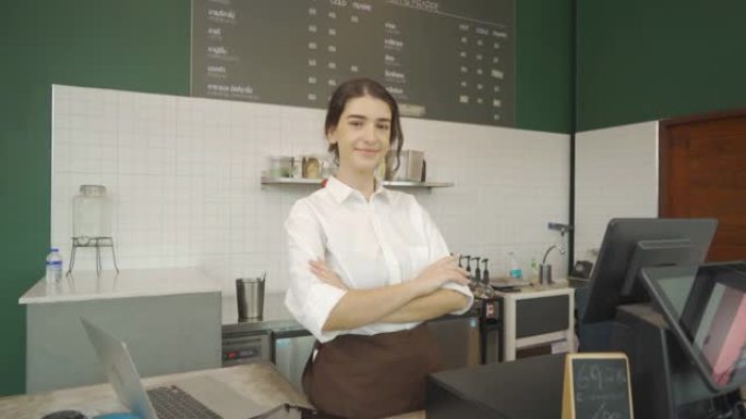 微笑着快乐的年轻中东女服务员穿着围裙，双臂交叉站着，咖啡厅收银员服务员的肖像。人们的生活方式。商务服