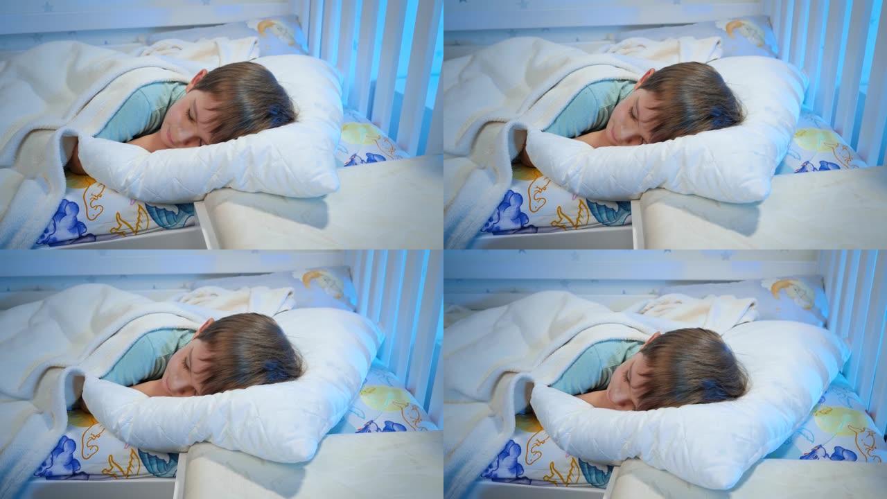 晚上穿着睡衣的小男孩在白色毯子下睡在床上的视频。孩子晚上休息和做好梦