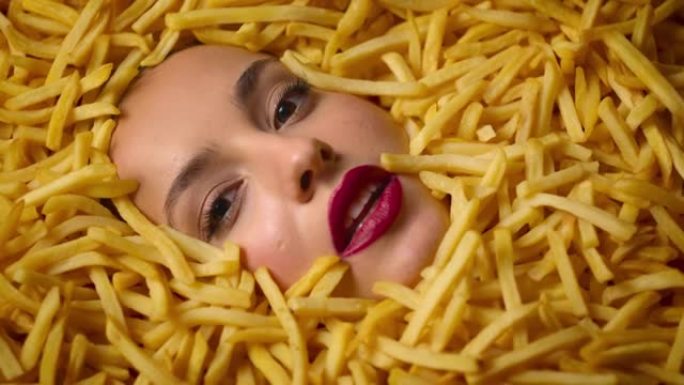 美女时装模特女孩躺在美味的薯条里。薯片化妆脸。