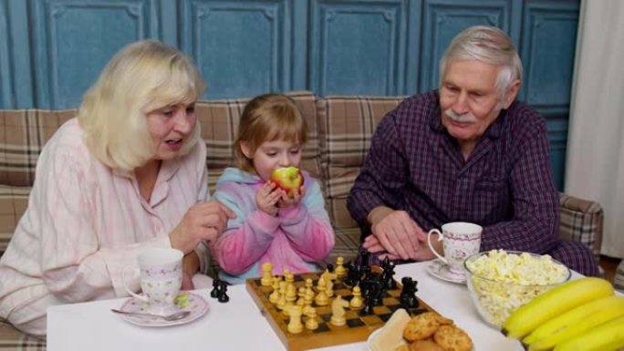 成熟的祖母祖父与女孩孙子在房间的桌子上下棋游戏