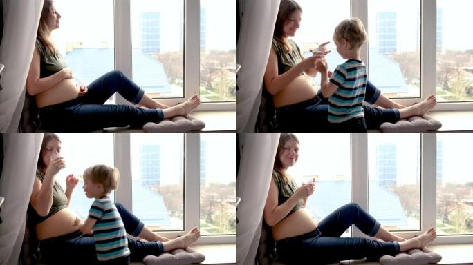 善举。怀孕的女人在窗户附近休息，她的小儿子给她一杯水，然后亲吻怀孕的母亲肚子。真正的家庭期待婴儿的时