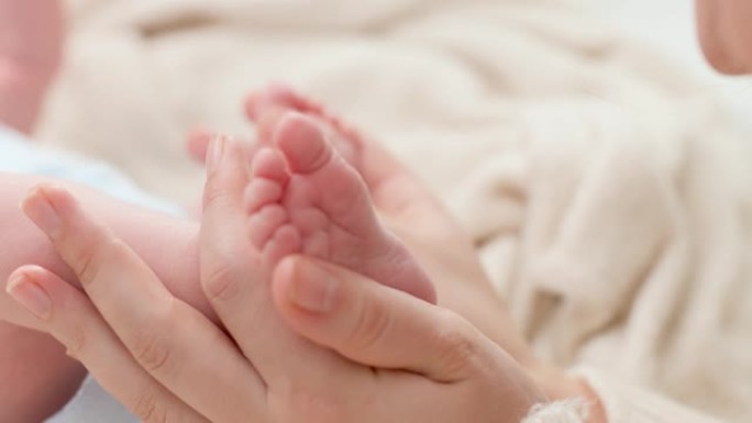 特写镜头，年轻的母亲轻轻地抱着并抚摸着躺在床上的新生男婴的小脚。家庭幸福与有小孩的父母的观念