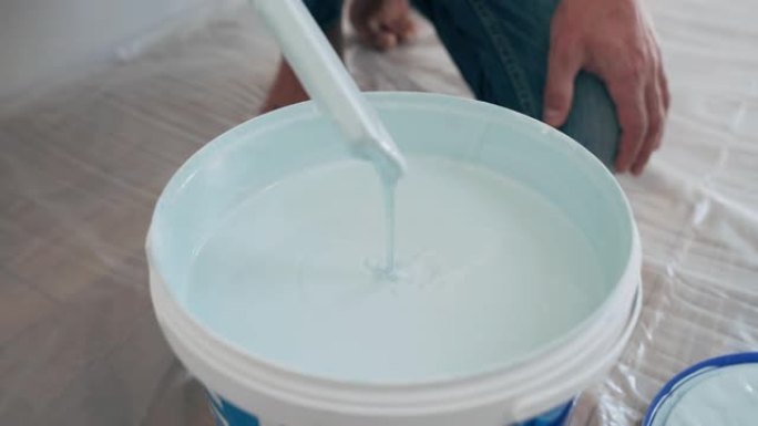 男人的手用棍子搅拌水桶里的油漆蓝色油漆滴入水桶家庭维修室修复施工侧视图