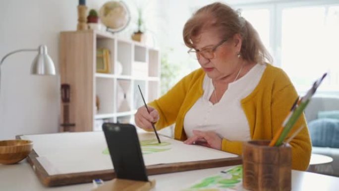 资深退休妇女使用智能手机进行水彩画在线课程