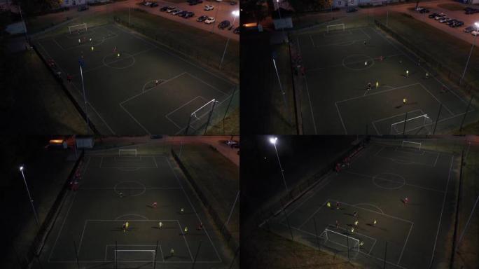 足球场的鸟瞰图，小男孩在夜间体育场踢足球。小男孩在夜间体育场鸟瞰图与教练踢足球。