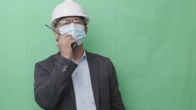 亚洲血统的男性专业人士或工程师，年龄40-50岁，穿防护服。使用绿色背景上的对讲机。