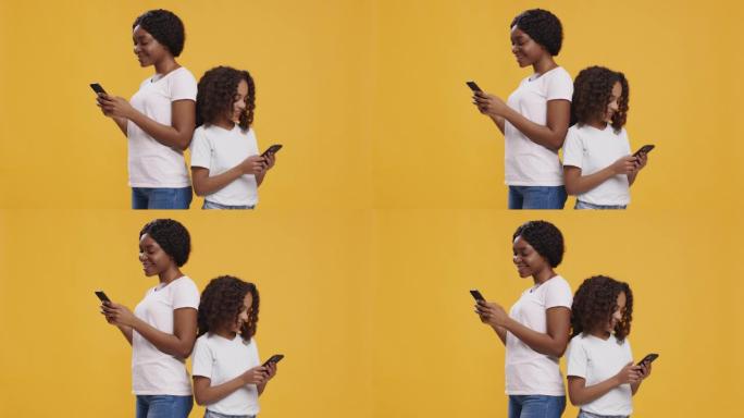 非裔美国人母女在智能手机上建立网络，背靠背站在orange studio背景上
