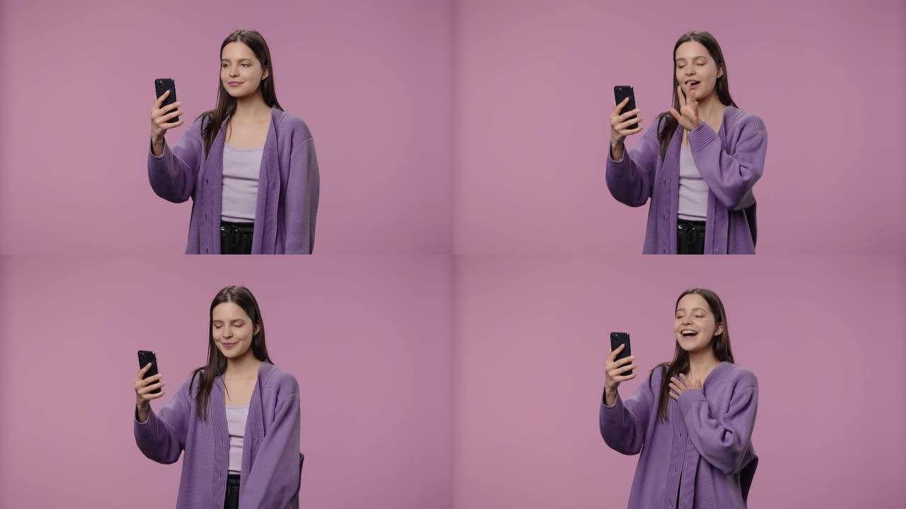 具有自然美的模特肖像正在使用智能手机进行视频通话。长发的年轻女孩在紫色工作室背景下摆姿势。特写。慢动