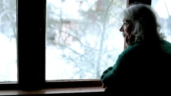 老年妇女站在窗前，独自望着远方。