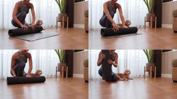 年轻的亚洲妇女展开卷黑色瑜伽垫，在家和她的狗玩瑜伽，检疫自己从新型冠状病毒肺炎