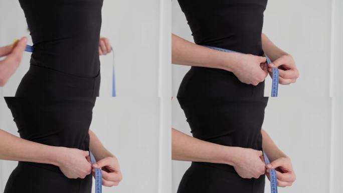 身材合身的女人测量腰部的特写镜头。年轻女性测量她的腰部。