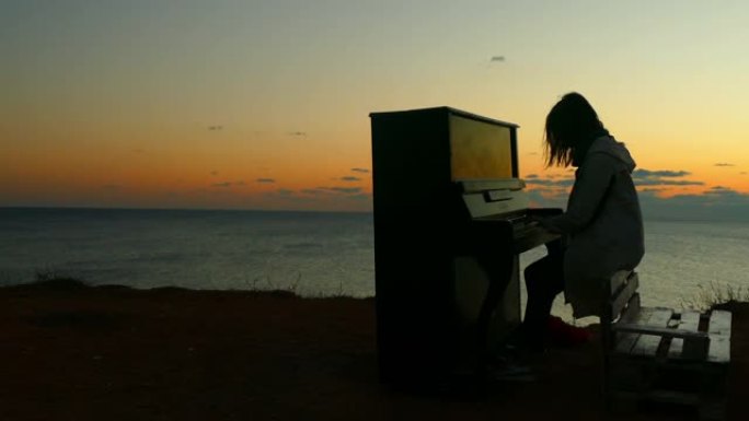 日落时在海滩上弹钢琴的女孩的剪影