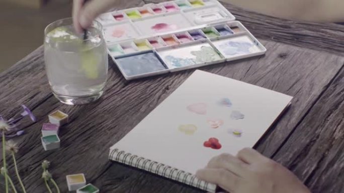 女人画一张彩色三色堇的卡片与水彩在检疫时间的新爱好。新常态生活中的自我保健和健康运动。