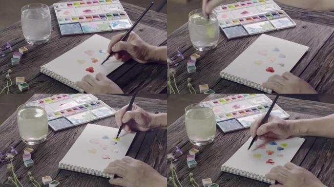女人画一张彩色三色堇的卡片与水彩在检疫时间的新爱好。新常态生活中的自我保健和健康运动。