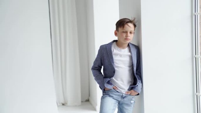 一个穿着夹克和牛仔裤的十几岁男孩站在窗户旁摆姿势。