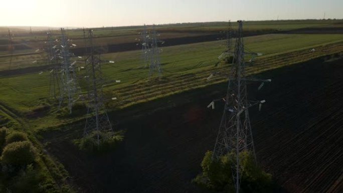 无人机飞越输电铁塔，在日落时支撑架空高压电力线