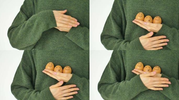 穿着绿色毛衣的年轻女性正在展示两个手绘鸡蛋，带有拟人化的笑脸，复活节准备，节日心情概念