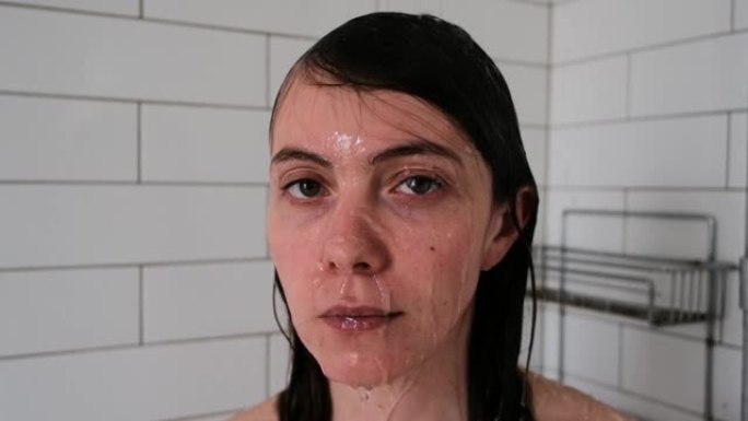 漂亮的黑发女人站在淋浴间的喷水口下