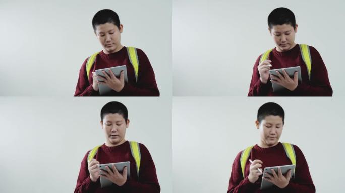 亚洲男生穿着毛衣在灰色背景的数字平板电脑上书写，教育生活方式理念。