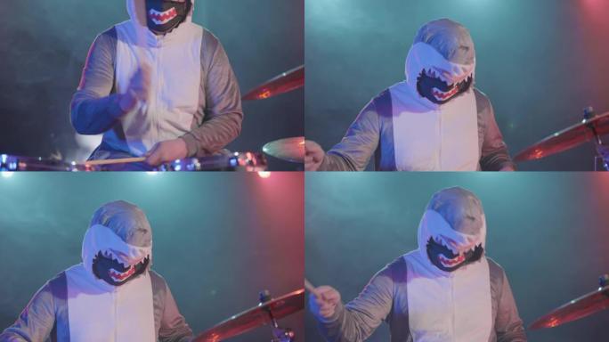 穿着节日鲨鱼服装的音乐家打鼓并击打敲击乐。一位音乐家在黑暗中伴随着明亮的灯光和烟雾的节日音乐会上演奏