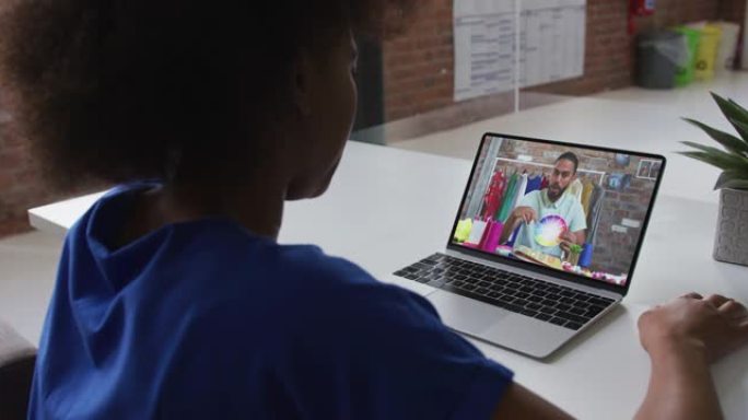 非裔美国妇女在办公室与男同事在笔记本电脑上进行视频通话的后视图