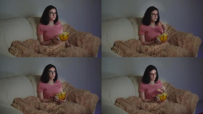戴着眼镜的漂亮黑发女孩在家里吃薯片看电视