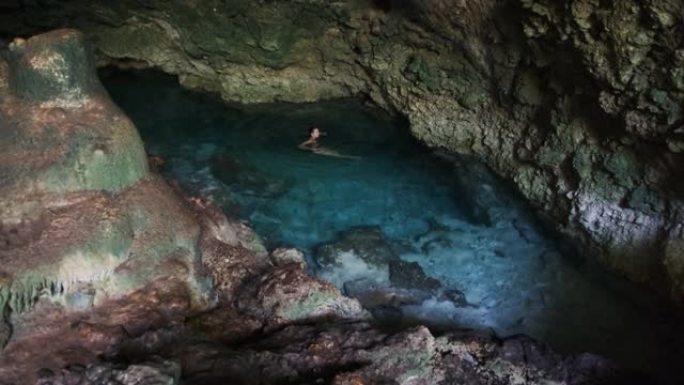 年轻女子在山洞的地下河中游泳，悬崖之间有淡水