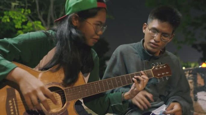 亚洲女孩正在学习如何弹吉他，从一个正在教她的朋友开始。
