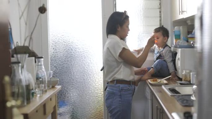 母亲在厨房给孩子喂饭。