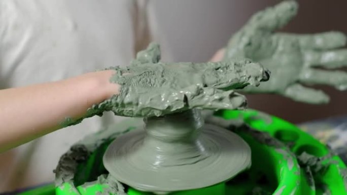 一个被粘土弄脏的七岁男孩正专注于在陶工的轮子上制作粘土产品。特写。4k