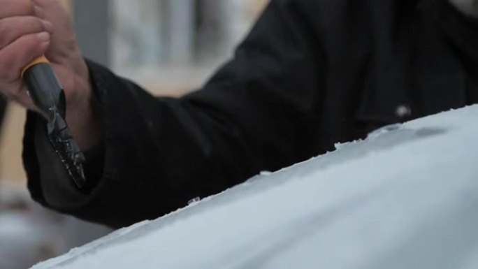 老人用刮冰机从雪地上清洗汽车引擎盖