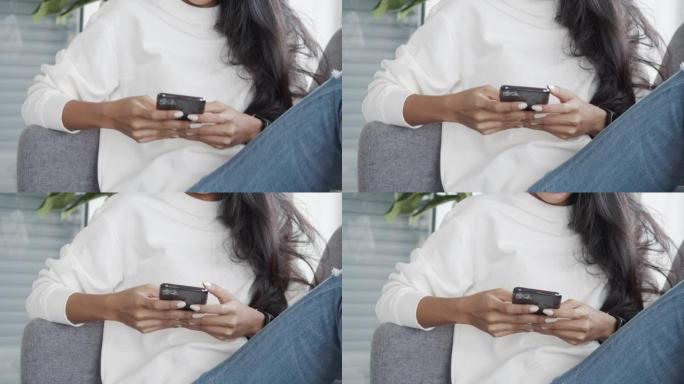 亚洲妇女坐在家里客厅的沙发上与朋友在线聊天。在智能手机上关闭女性打字信息。