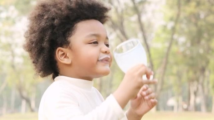 可爱的黑人孩子从杯子里喝牛奶，嘴里舔着美味，慢动作镜头。