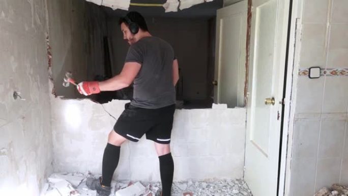 年轻人用槌打破墙壁。房屋装修。