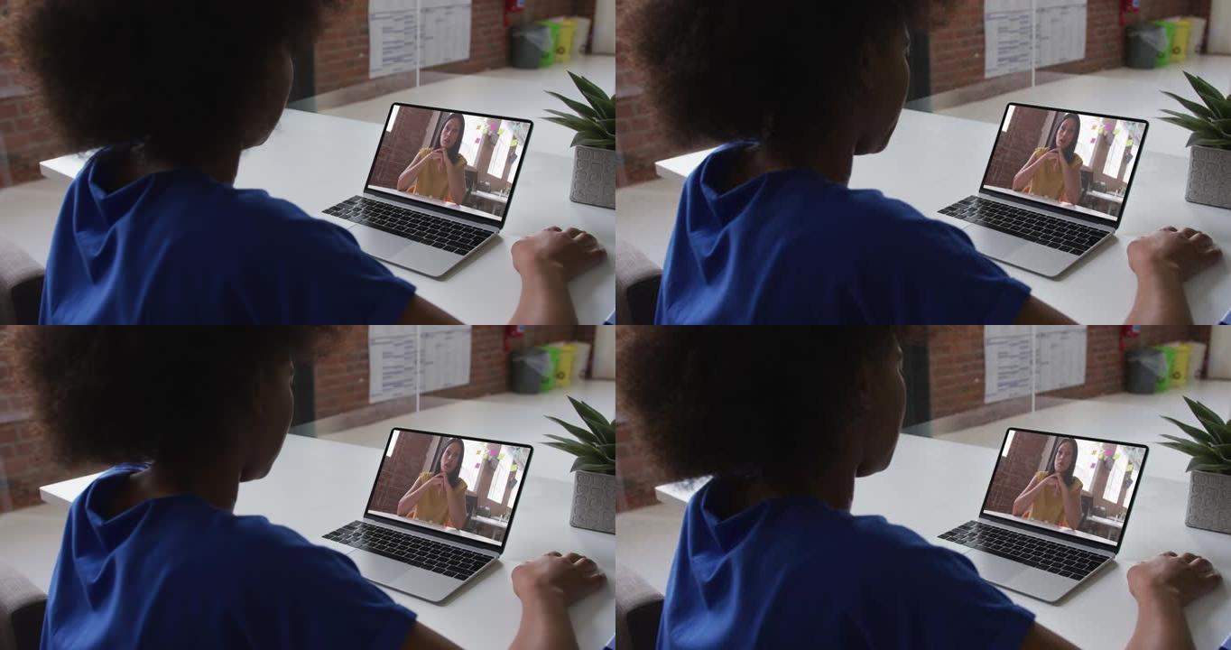 非裔美国妇女在办公室与女同事在笔记本电脑上进行视频通话的后视图