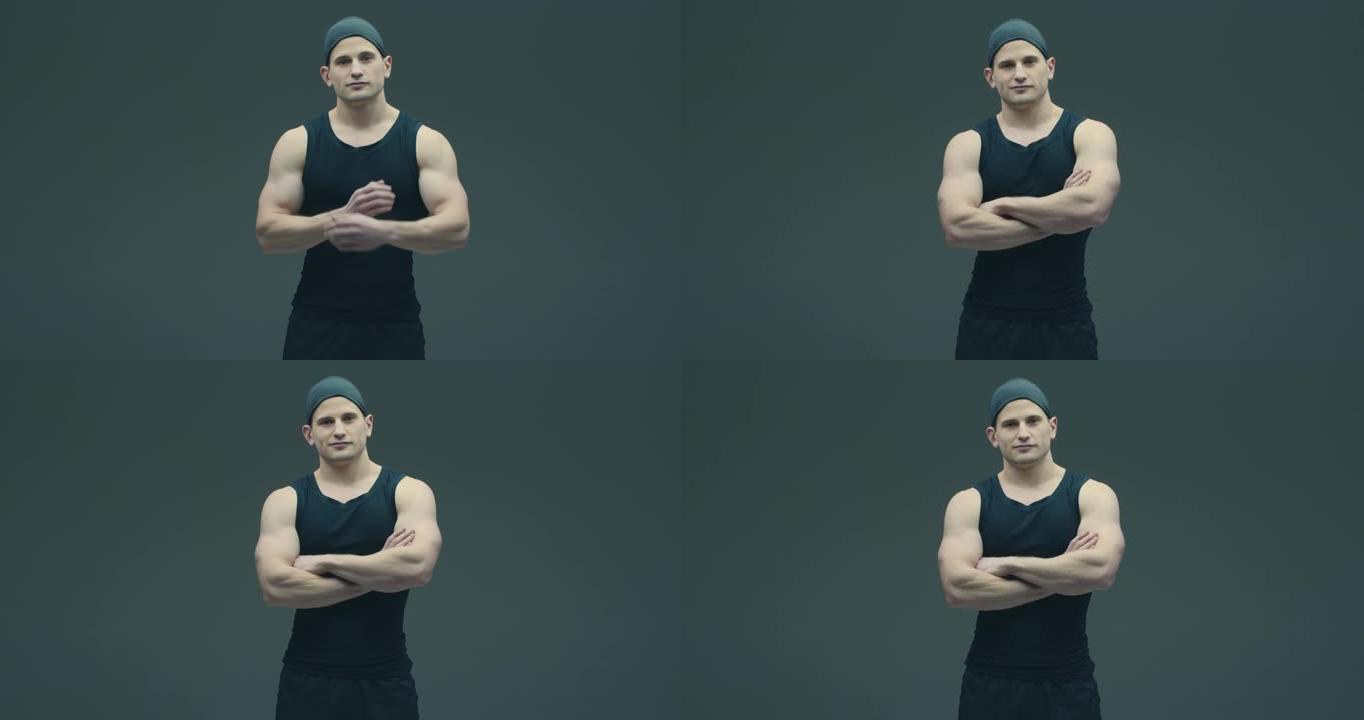 4k视频运动年轻帅哥健身教练折叠手在胸部在灰色工作室背景，复制空间