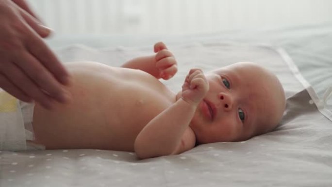母亲用男婴做简单的运动，使婴儿骨骼和肌肉更强壮，新生儿躺在床上靠窗。