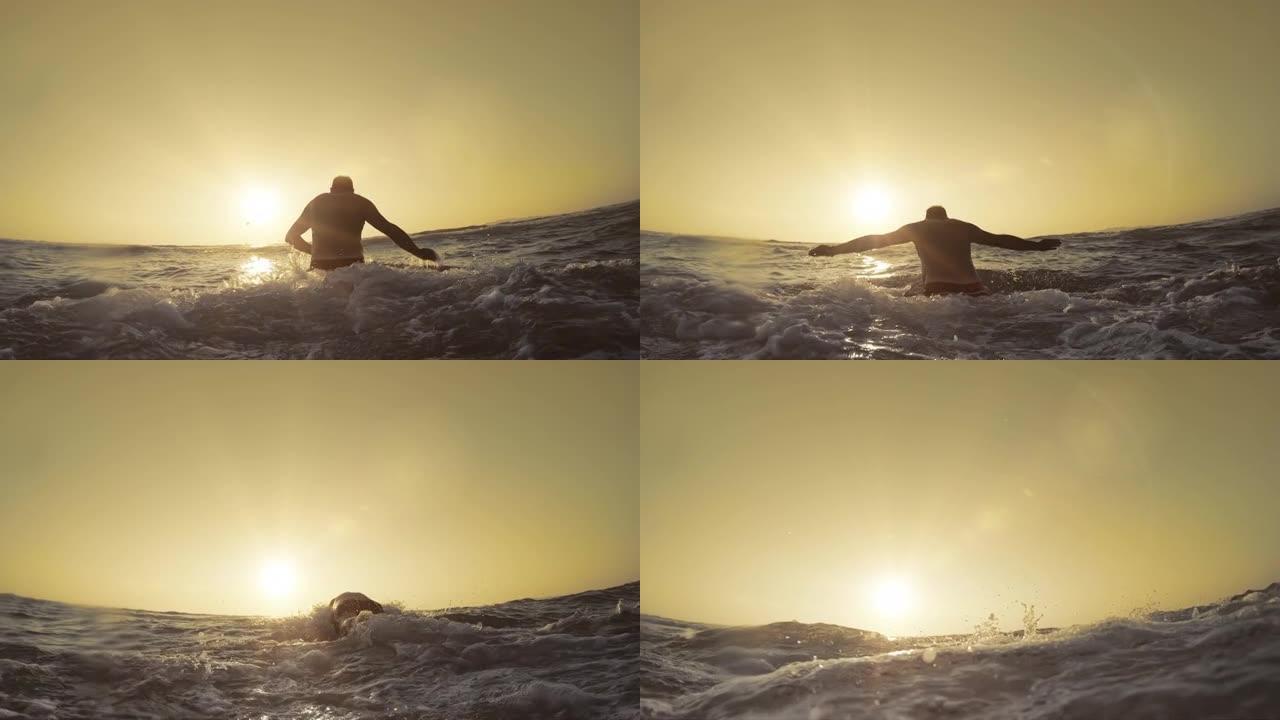 男子在浅水的沙滩上奔跑，在日落时跳着游泳，慢动作