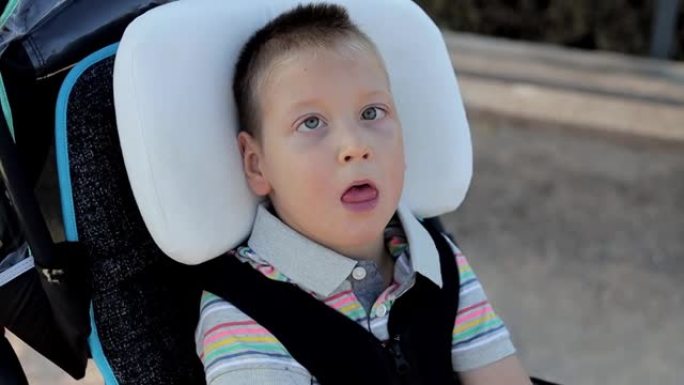 特写坐在户外特殊轮椅上的小孩。身体残疾儿童