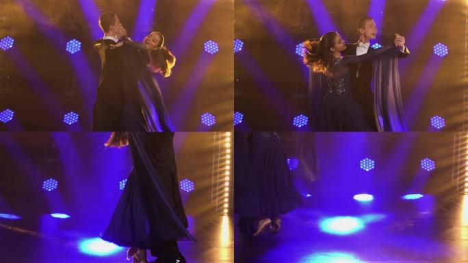 优雅的舞厅舞者夫妇跳舞华尔兹元素弹跳和牵手。一男一女在明亮的蓝色聚光灯和烟雾中，在黑暗的工作室里华尔