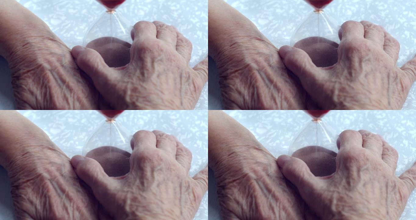 特写布满皱纹的老人用静脉和指甲的手握住沙漏
