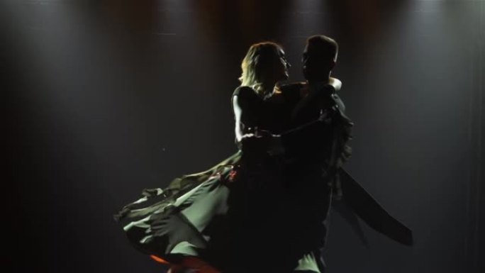 一个男人和他的伴侣女人跳华尔兹，在空中盘旋。舞会上一对剪影的舞厅舞者，被明亮的光线照亮。特写。慢动作
