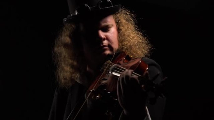 爱尔兰风格的原始帽子上的男人肖像在黑色背景上拉小提琴。小提琴手熟练地操纵小提琴弓，在黑暗的工作室里演