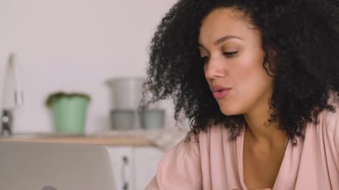 可爱的非洲裔美国妇女使用手机进行视频通话。黑色黑发女人坐在明亮厨房的桌子旁摆姿势。特写。慢动作就绪，