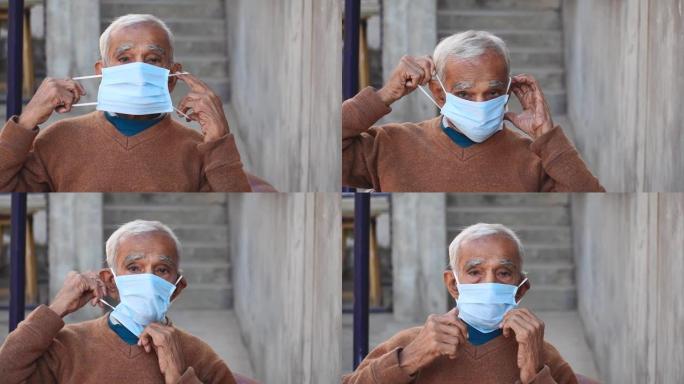 坐在室内时戴着面具的印度老人的肖像竖起大拇指。在电晕病毒大流行2021年期间