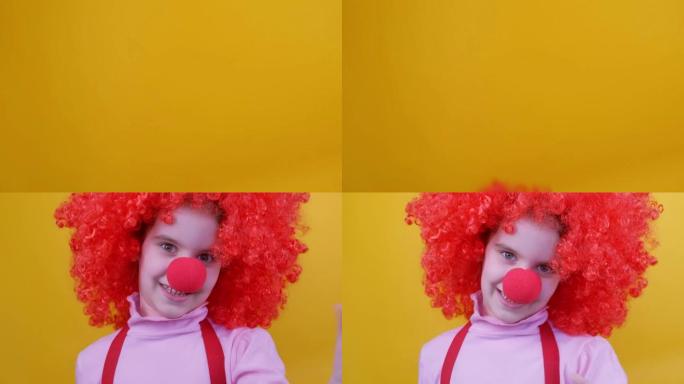 有趣的小丑女孩，红色鼻子和头发的孩子在黄色背景上跳跃和大笑。4月1日愚人节，生日概念。