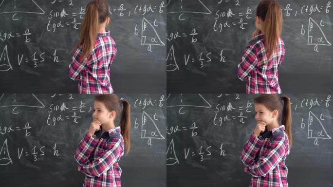 穿着衬衫的高加索女孩女学生站在带有公式的粉笔板的背景下。试着解决这个等式，微笑着。复制空间。