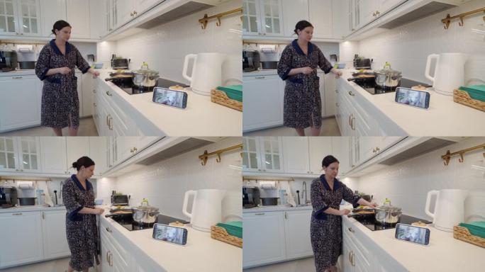 妈妈在厨房里用ip摄像头作为手机上的婴儿视频监视器做饭，女人在智能手机屏幕上实时观看熟睡的婴儿