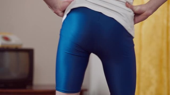 蓝色运动打底裤在室内旋转的男性臀部特写。无法辨认的瘦瘦的白人年轻人在80年代90年代的家中锻炼。运动