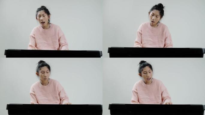穿着粉红色毛衣的快乐亚洲女孩在灰色背景上学习玩电动键盘，生活方式概念。